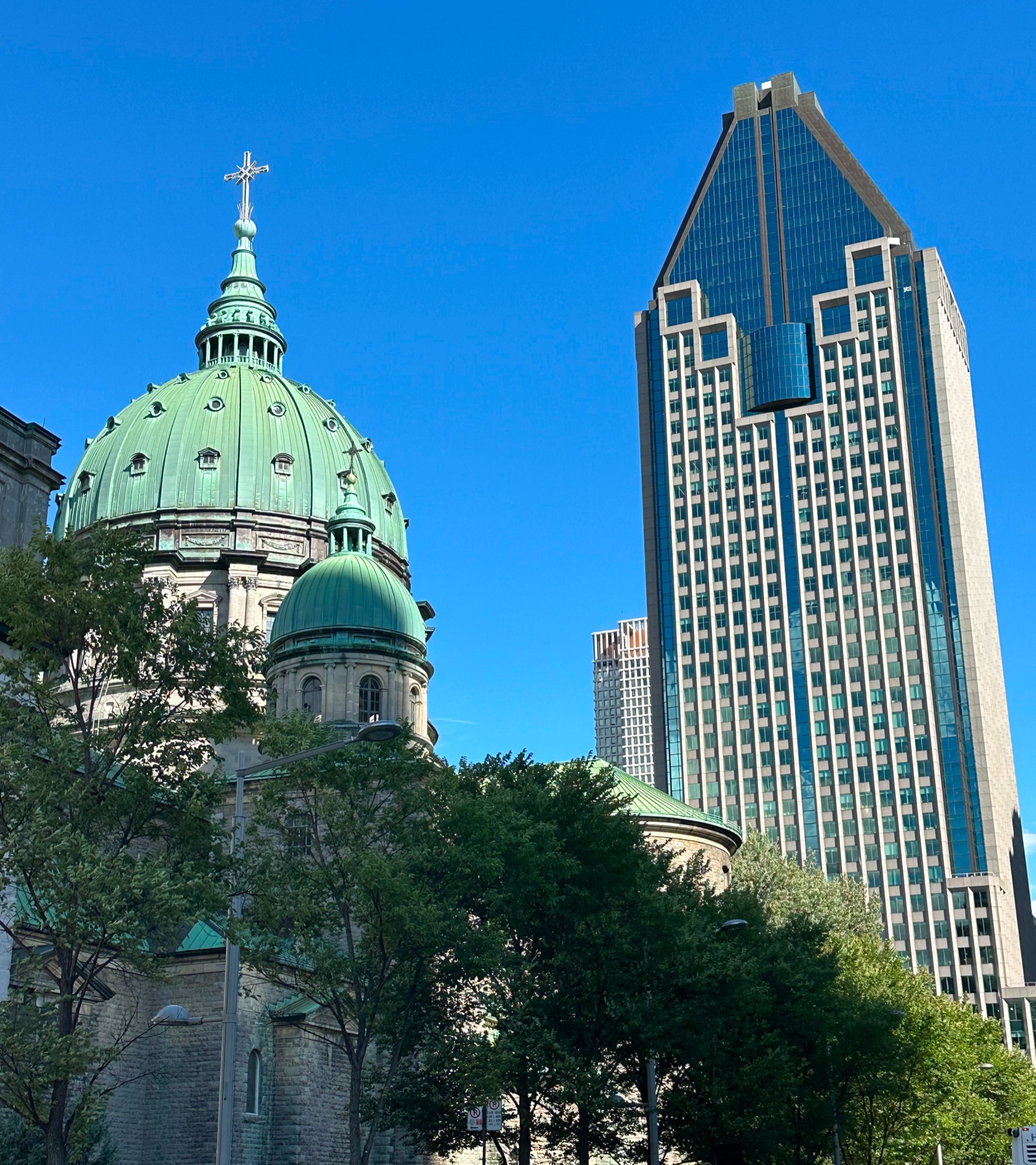 An old copper-domed church beside a modern glass high-rise in Montreal